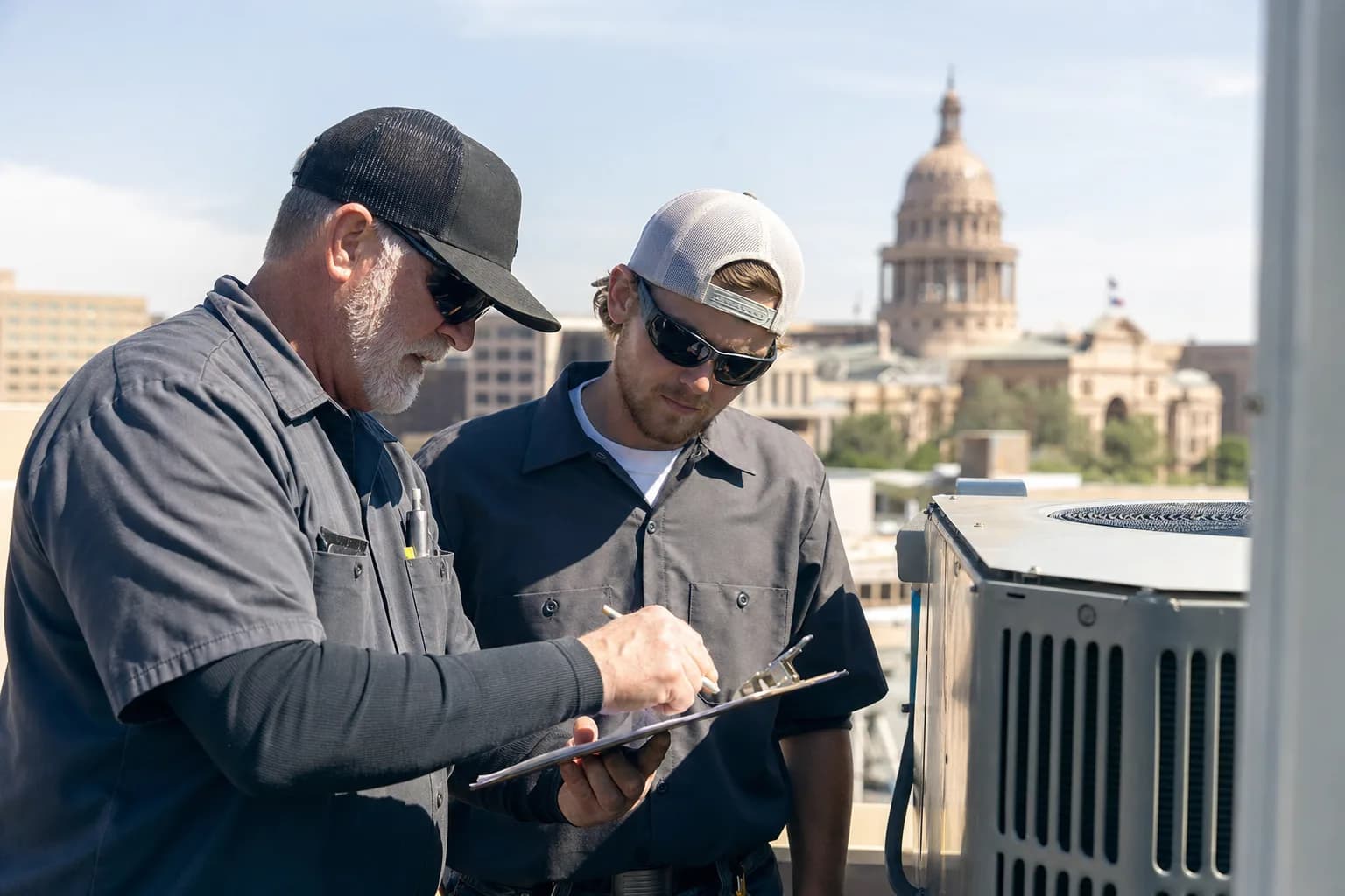 Two HVAC professionals consulting beside a commercial rooftop unit in Texas